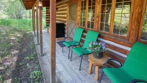 Eine Holzhütte mit einer Veranda, grünen Stühlen und einem Tisch mit einem Blumentopf.