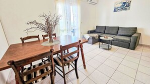 A dining area with a wooden table and chairs, a grey sofa, and a small round table with a decorative item. - Apartment Antun by Interhome (Korčula/Prigradica)
