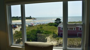 Una habitación con un gran ventanal con vistas a una playa, una silla y un edificio rojo al fondo.