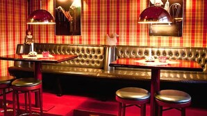 Een restaurant met rode geruite behang, een lederen bank en twee barkrukken.