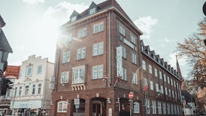 Een hotel in een stad, gebouwd van rode bakstenen, met veel ramen, een bord dat een zone van 30 aangeeft, en vlaggen.