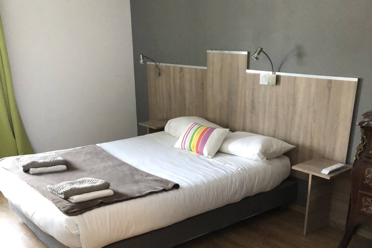Un dormitorio moderno con cabecera de madera, una cama grande con ropa de cama blanca, una mesita de noche y un velador.