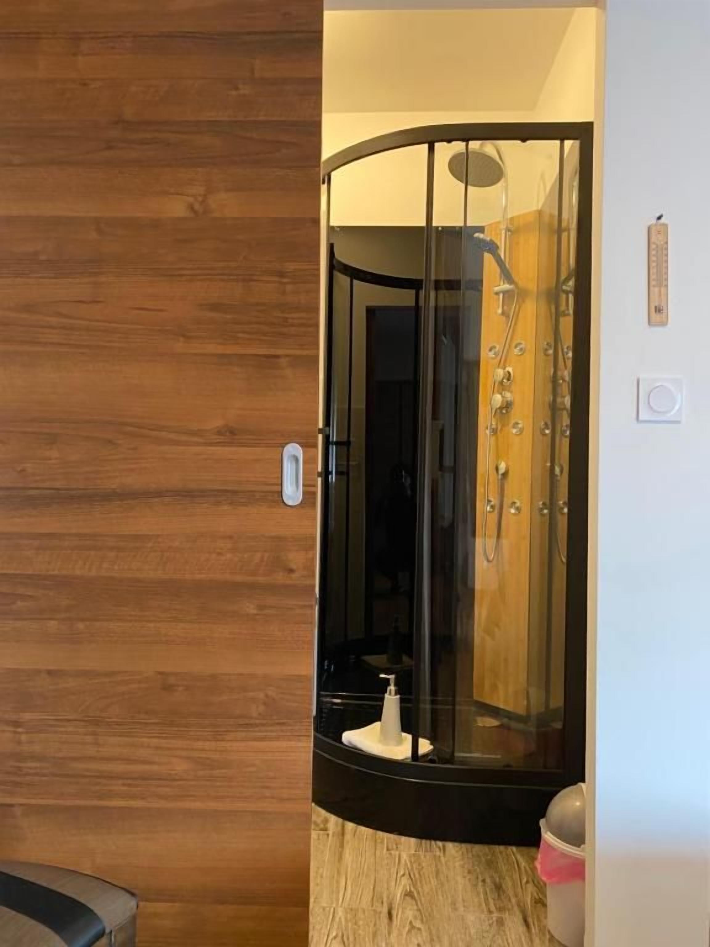 Une salle de bain moderne dotée d’une paroi de douche en verre incurvé, d’un mur en bois et d’un espace douche bien délimité.