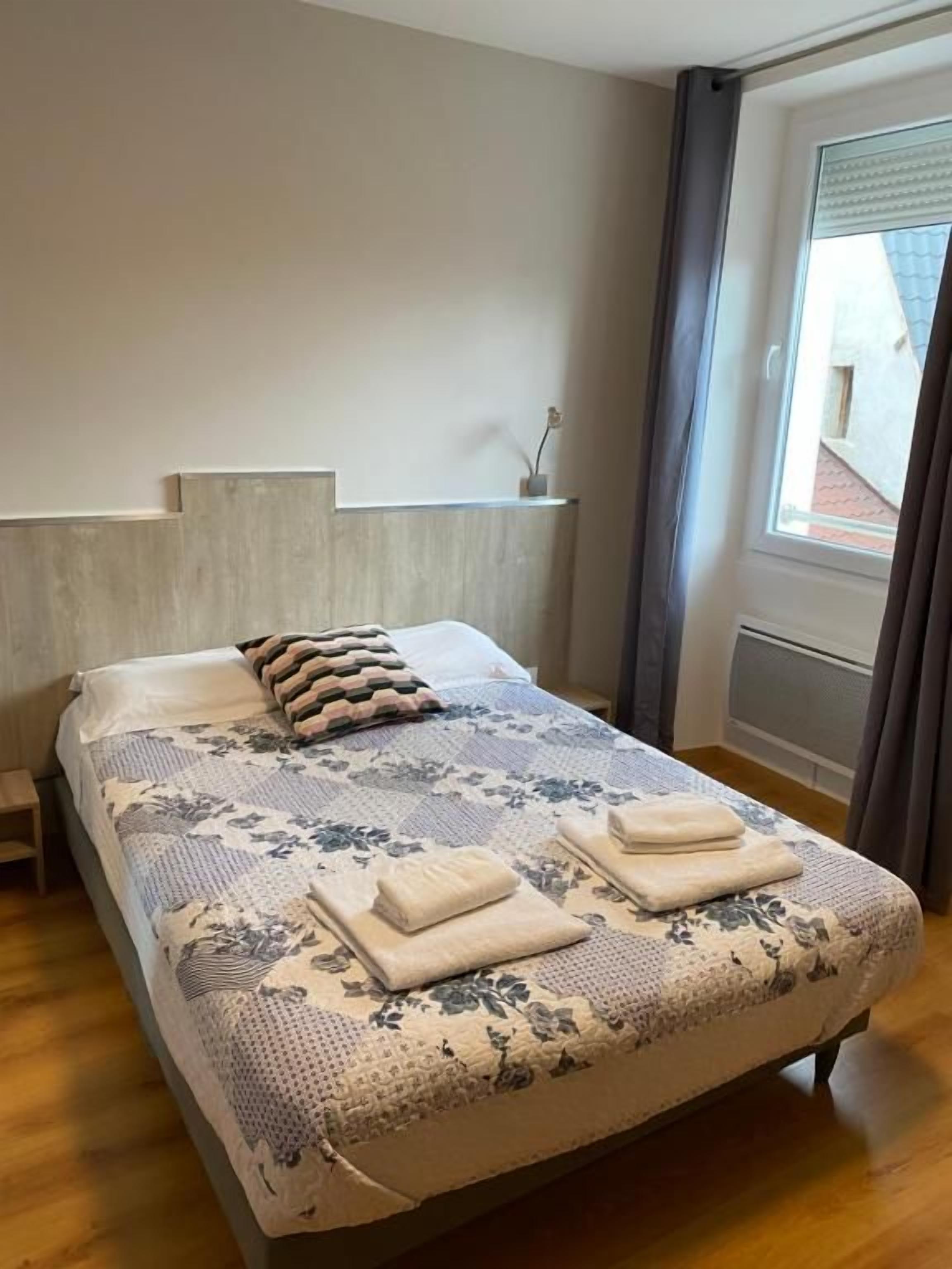 Un lit bien fait, avec une couvre-lit à motifs et des oreillers, une table de chevet et une fenêtre avec des rideaux.