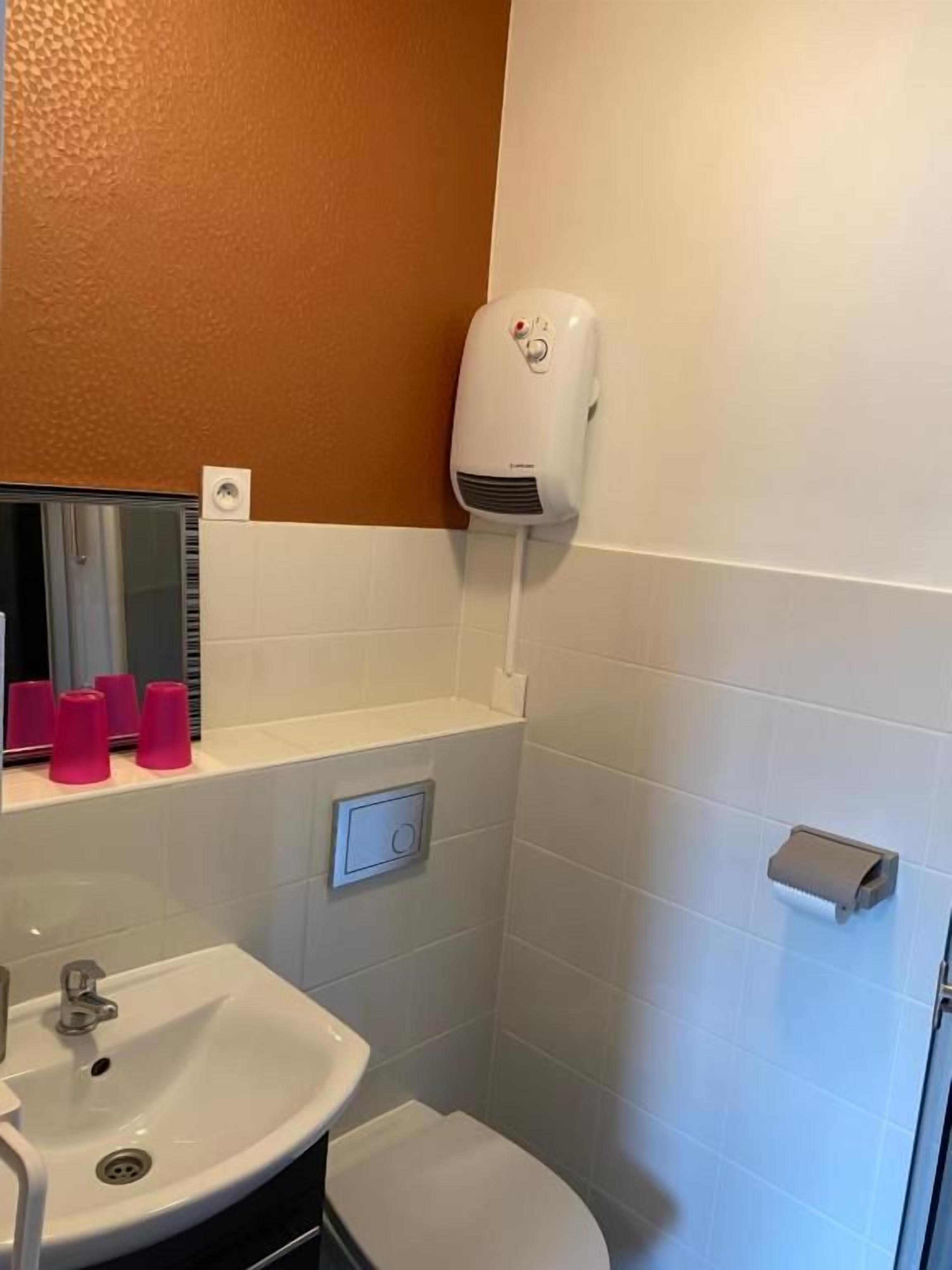 A bathroom with a white sink, a toilet, and a hand dryer mounted on the wall.