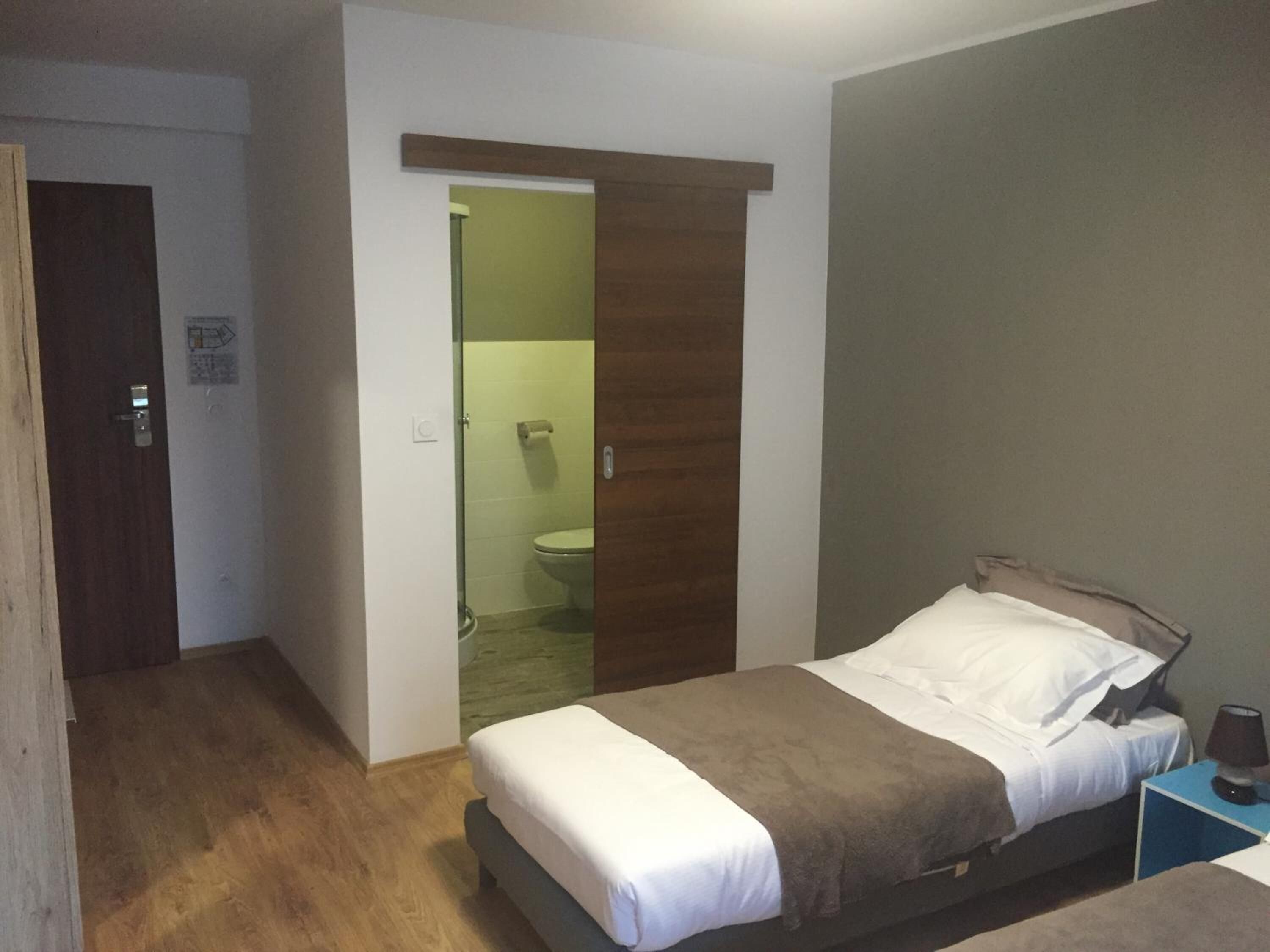 Une petite chambre à coucher, bien rangée, avec un lit, une table de chevet et une commode.