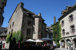 A stone building with a balcony and flower boxes, surrounded by other buildings. - Chalets Bois Moulin de Chaules (Saint-Constant-Fournoulès)