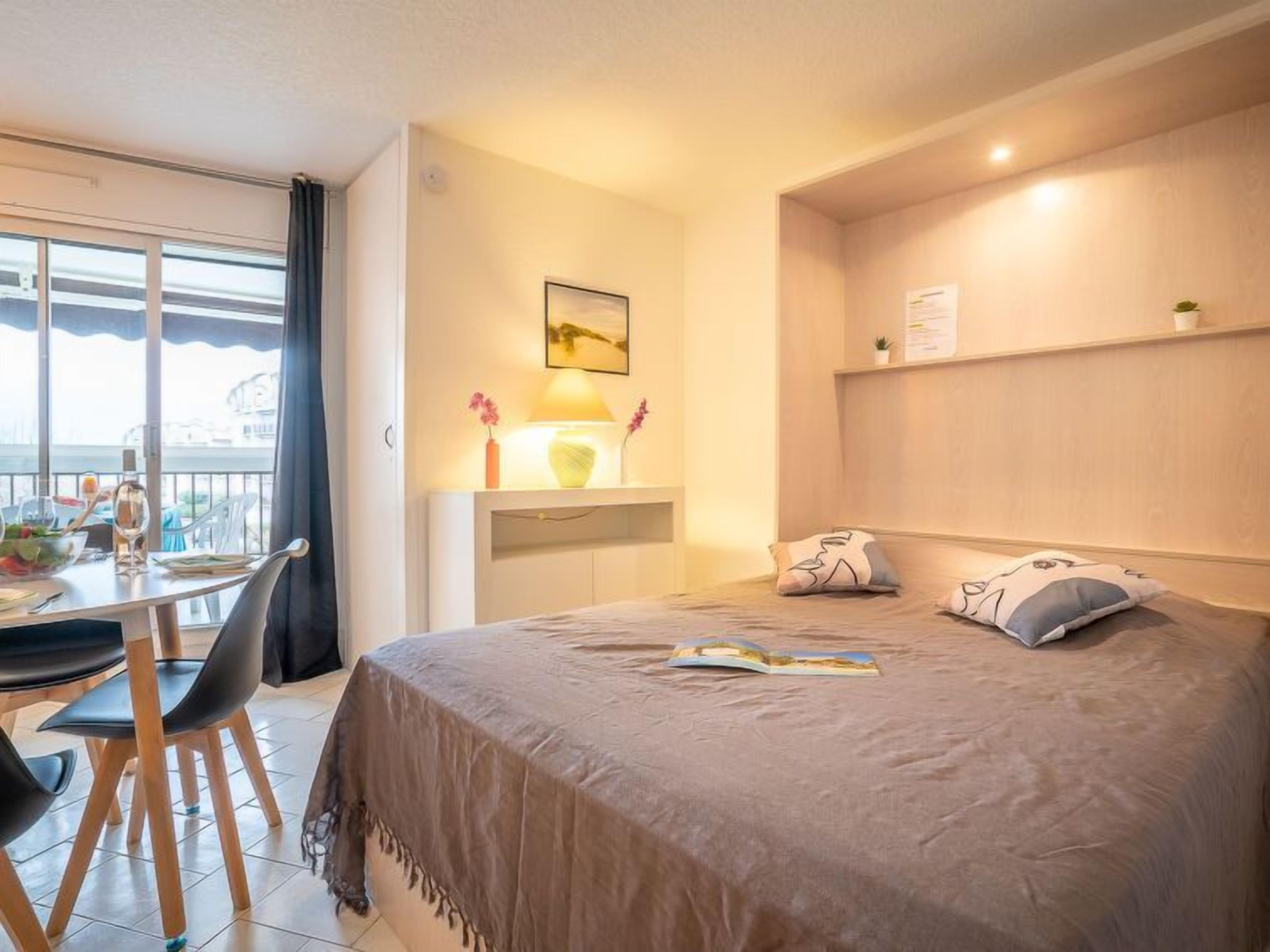 A bedroom with a bed, bedside table, lamp, and a view of the city through the window.