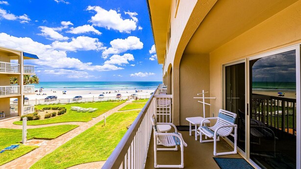 Un balcon avec vue sur la plage, des sièges à l’extérieur et un ciel dégagé.