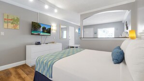 A bedroom with a bed, a TV, a dresser, a mirror, and a window.