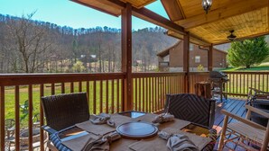 Un'area pranzo all'aperto coperta con sedie in vimini e un tavolo apparecchiato per due, con vista su un paesaggio boschivo.