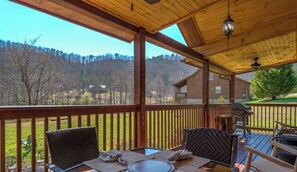 A covered outdoor dining area with wicker chairs and a table set for two, overlooking a forested landscape. - Two Bedroom Cabin Rental- Wears Valley-Near National Park- Seasonal Pool Access (Sevierville)
