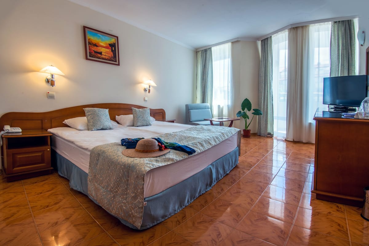 A hotel room with a large bed, two bedside lamps, a television, a desk, and a window with curtains.