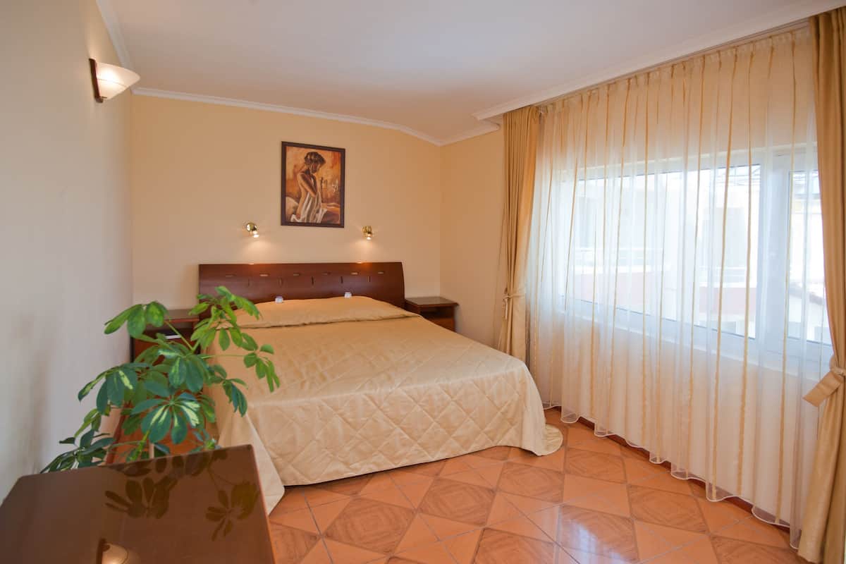 A bedroom with a bed, a nightstand, a lamp, a plant, and a painting on the wall.