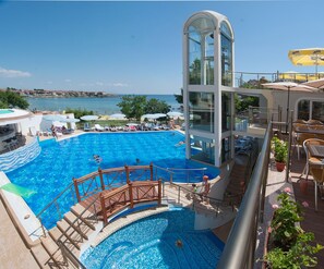 A large outdoor swimming pool with a glass elevator, lounge chairs, and umbrellas. - Villa List Hotel (Sozopol)
