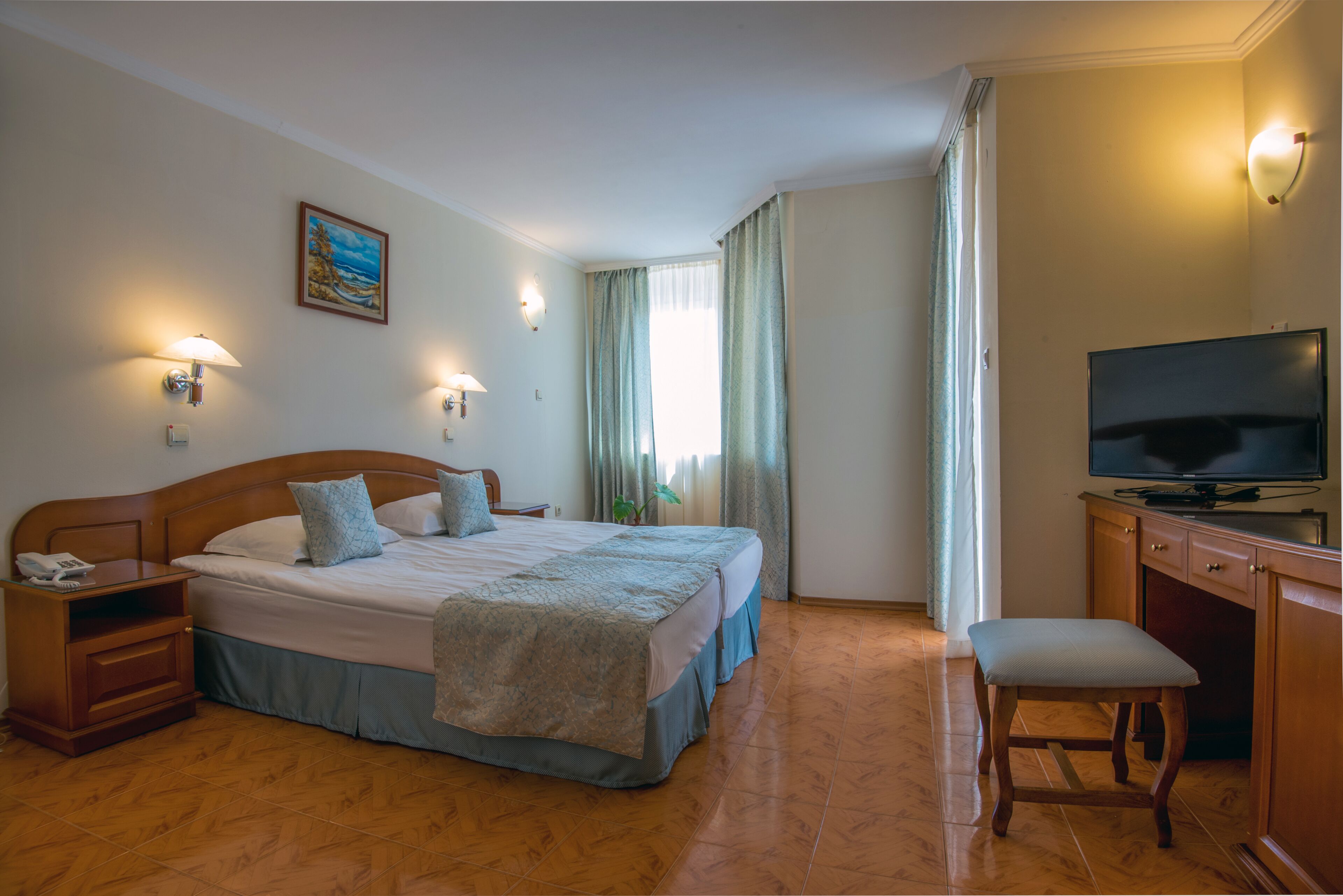 A hotel room with a large bed, bedside tables, a desk with a television, and a chair.