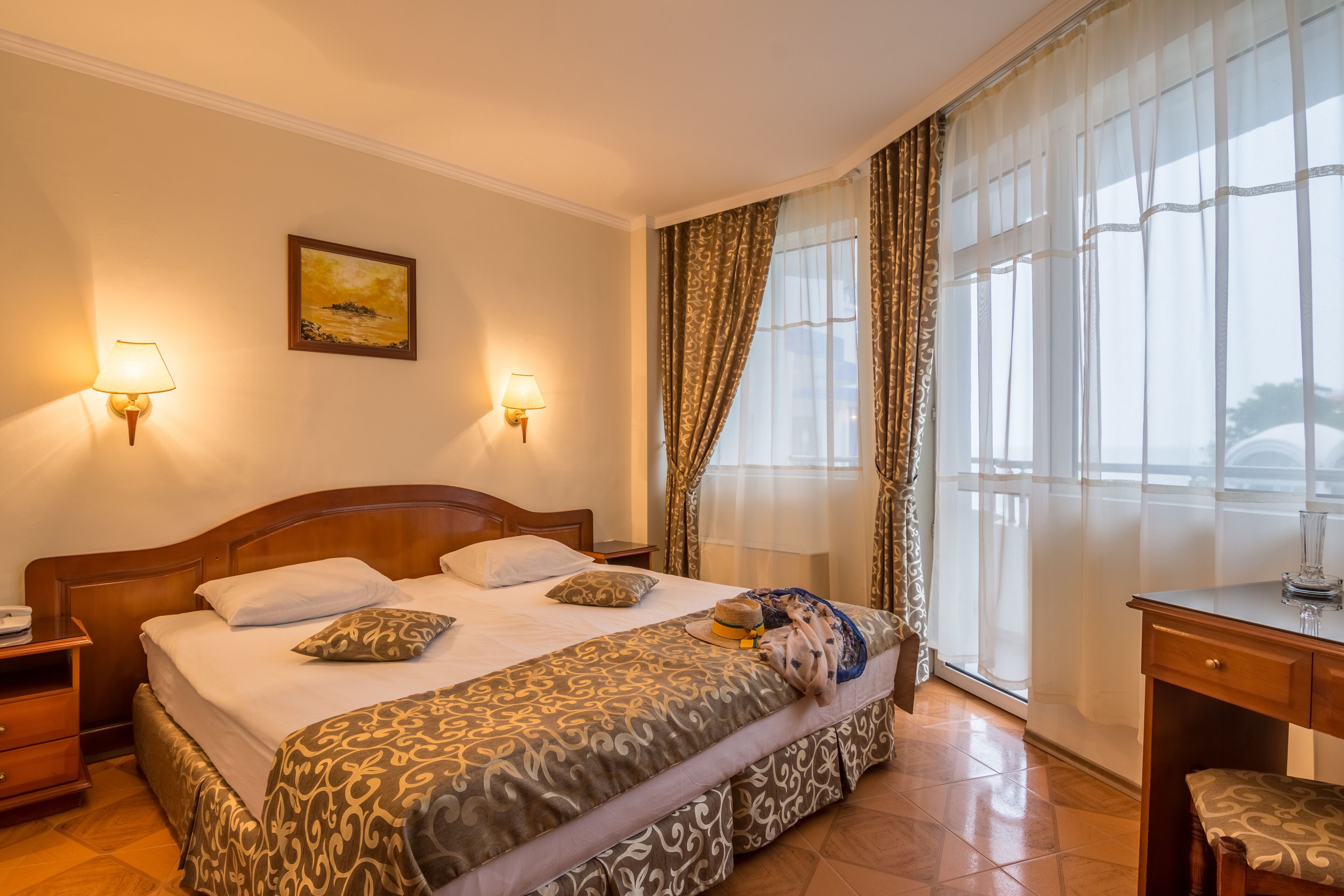 A hotel room with a large bed, two bedside lamps, a desk, and a chair.
