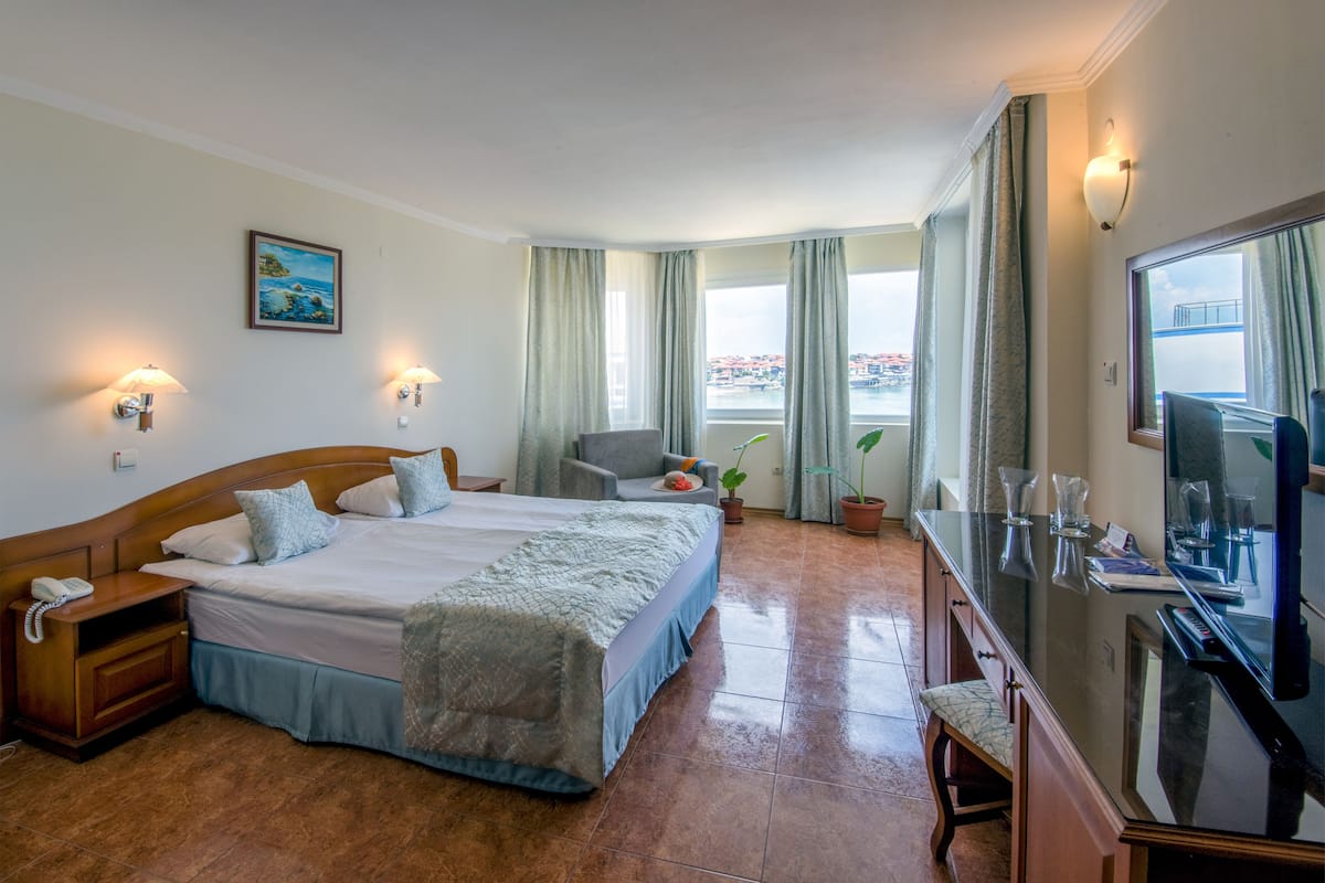 A hotel room with a large bed, a desk with a computer, a TV, and a window with curtains.