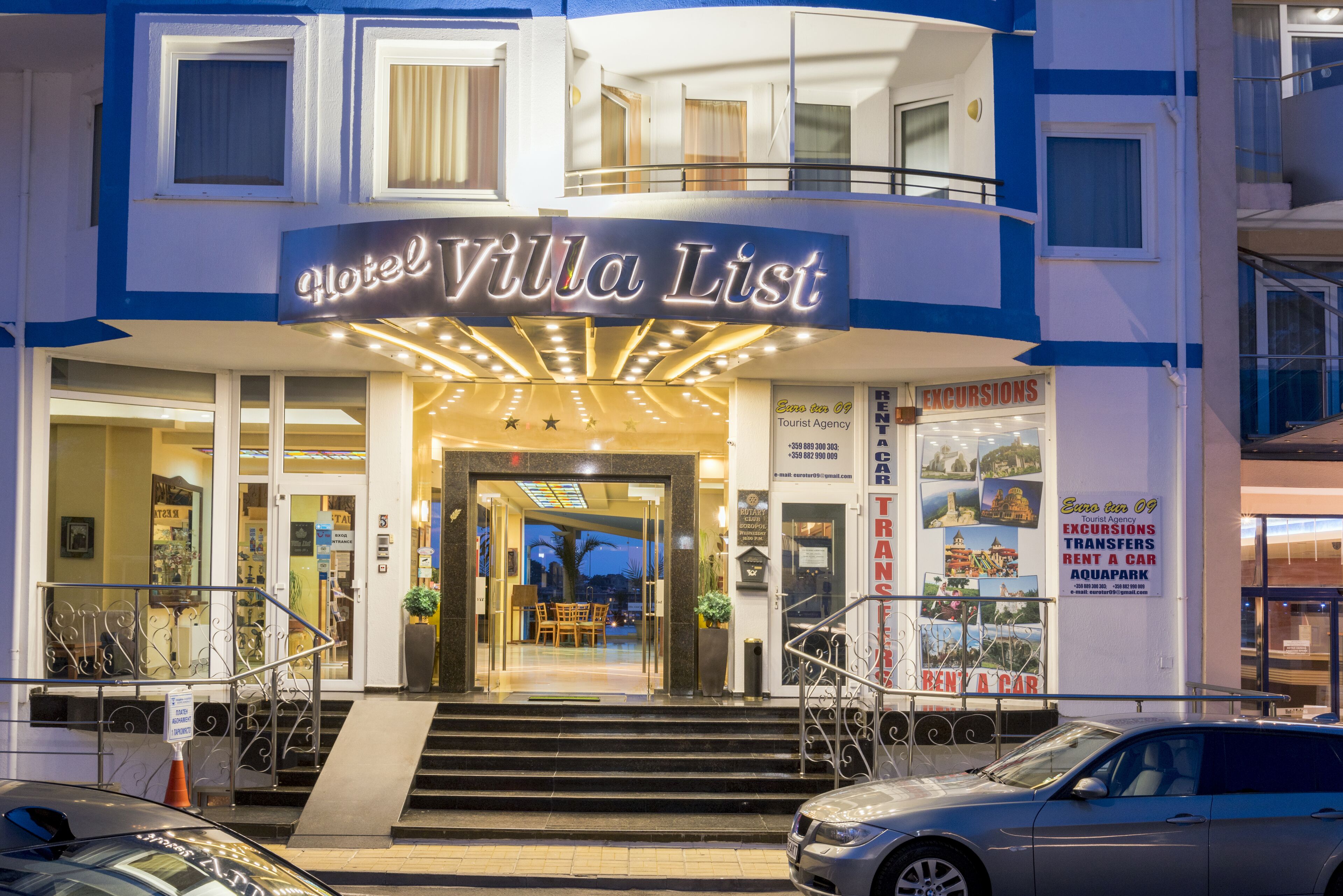 Entrada de hotel con un cartel que dice "Hotel Villa List", una escalera y una agencia de alquiler de coches cerca.