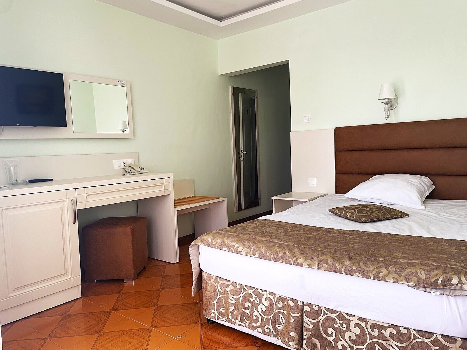 Une chambre d’hôtel avec un lit, un bureau, une chaise, une télévision et une porte.