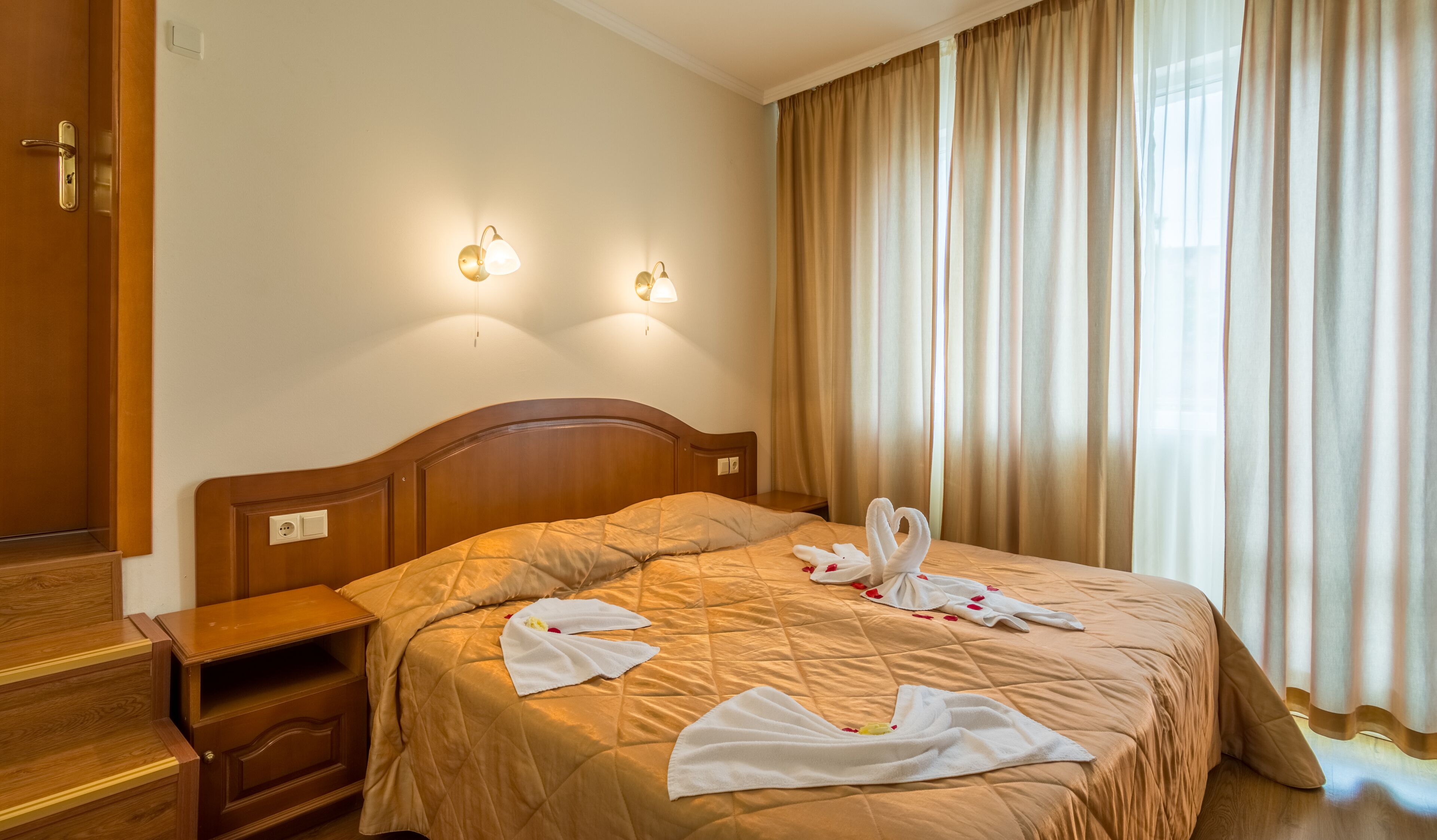 Une chambre d’hôtel avec un lit en bois, deux lampes de chevet, une table de chevet et une fenêtre avec des rideaux.