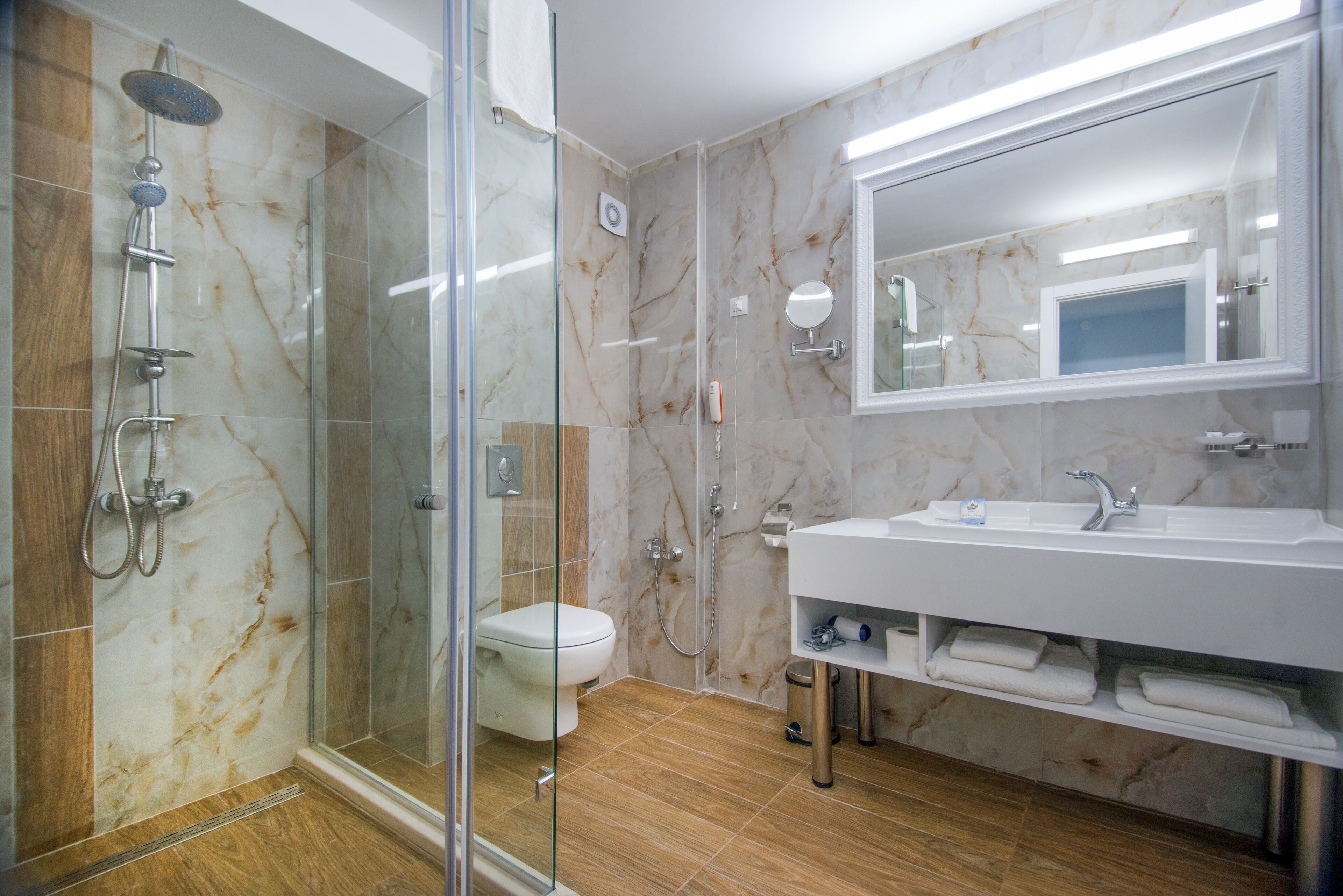 A modern bathroom with a glass-enclosed shower, a toilet, a large mirror, and a vanity with a sink and towel racks.