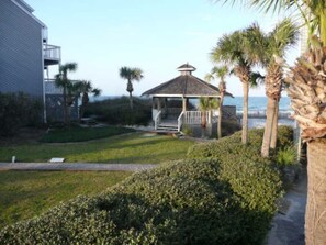 A gazebo with a porch, surrounded by palm trees and a grassy area.