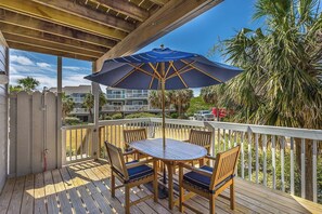 A wooden deck with a round table and chairs, a blue umbrella, and a view of a residential area with palm trees and a building in the background. - Gulf-View Townhome·Dog Friendly·Steps to Beach (Port Saint Joe)