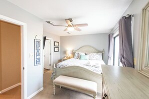 A bedroom with a bed, a bench, a ceiling fan, and a window with curtains.