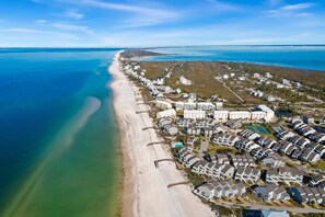 An aerial view of a coastal residential area with beachfront properties, a large hotel complex, and a clear view of the ocean.