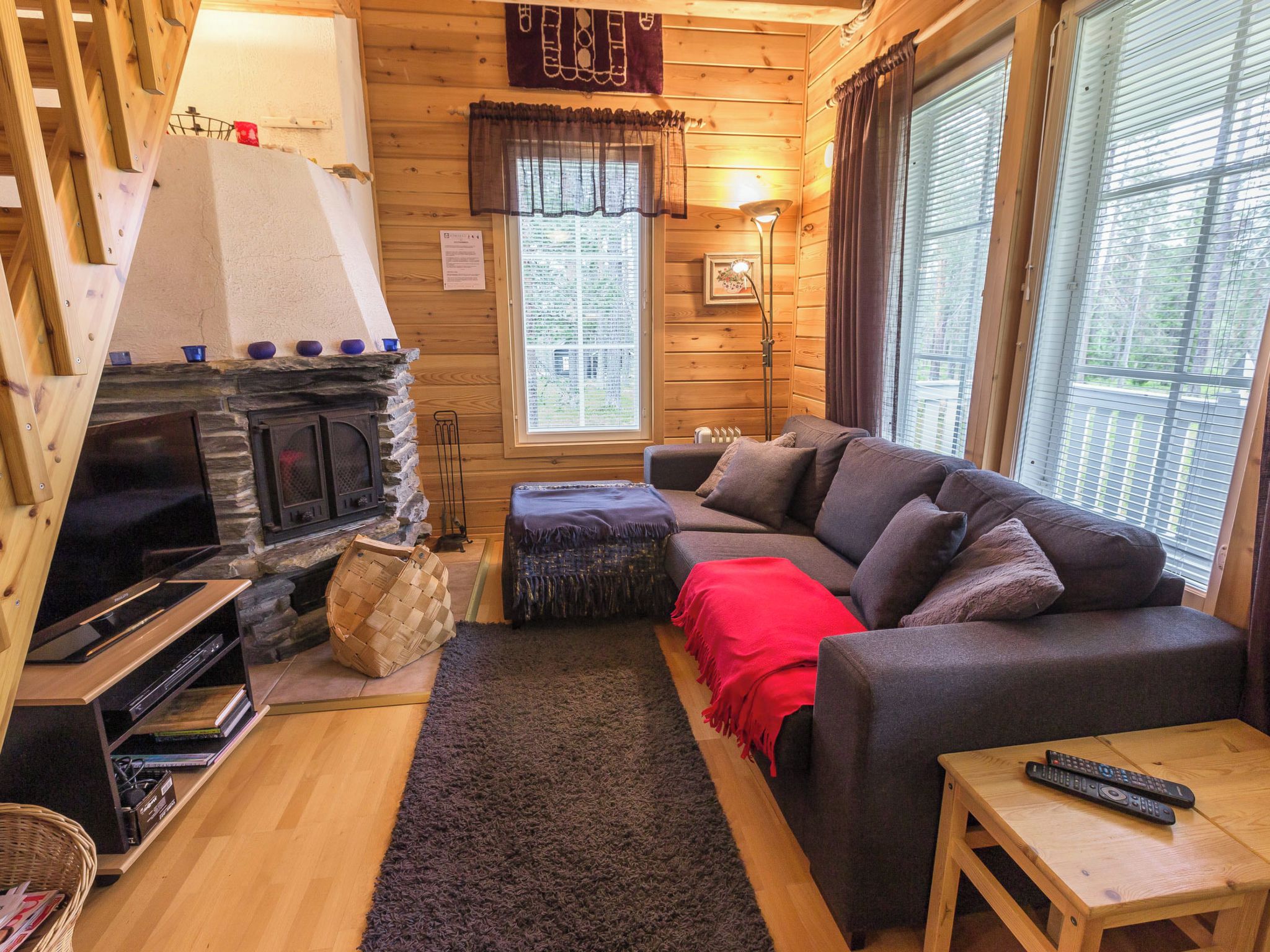 Ein gemütliches Blockhaus-Interieur mit Kamin, Sofa, Fernseher und Fenster mit Jalousien.