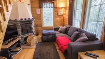 Ein gemütliches Blockhaus-Interieur mit Kamin, Sofa, Fernseher und Fenster mit Jalousien.