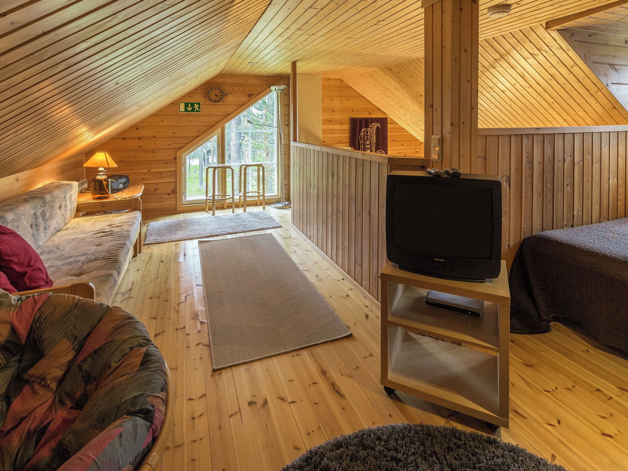 Ein gemütliches Blockhaus-Interieur mit Holzboden, einer Couch, einem Fernseher auf einem Schrank und einem Fenster mit Blick auf einen Wald.