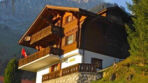 Et chalet-lignende hus med stensokkel, træbalkoner og et flag.