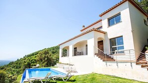 Una casa moderna de dos pisos con piscina, una escalera que lleva al nivel superior y vistas de la vegetación circundante.