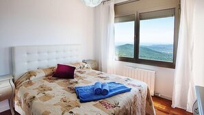 Un dormitorio con una cama grande, un cabecero blanco, una ventana con vistas al campo y una lámpara colgante.