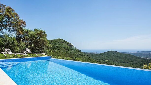 Una piscina infinita de color azul intenso, con sillones de descanso y vistas a colinas verdes.