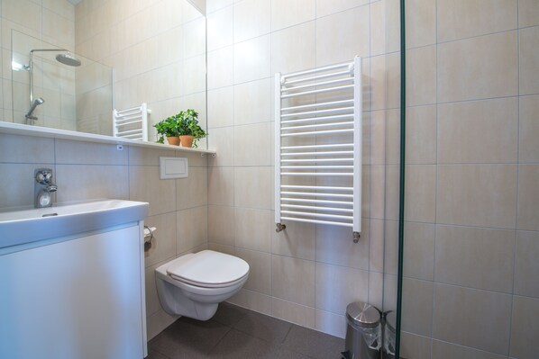 A bathroom with a toilet, sink, mirror, towel rack, and a potted plant.