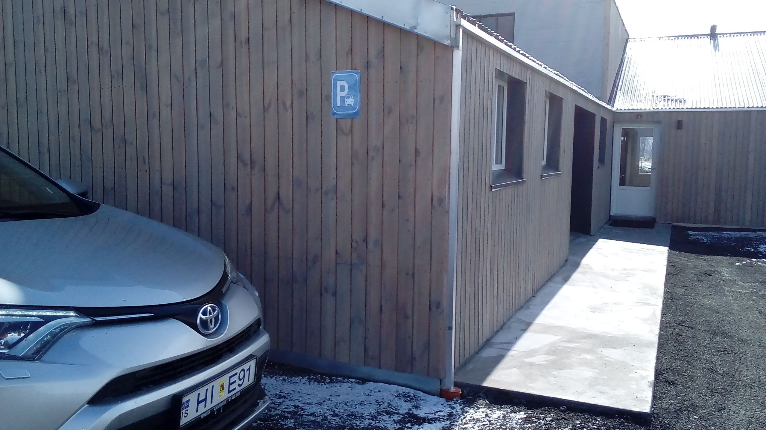 A car parked in front of a building with a wooden facade and a parking sign.