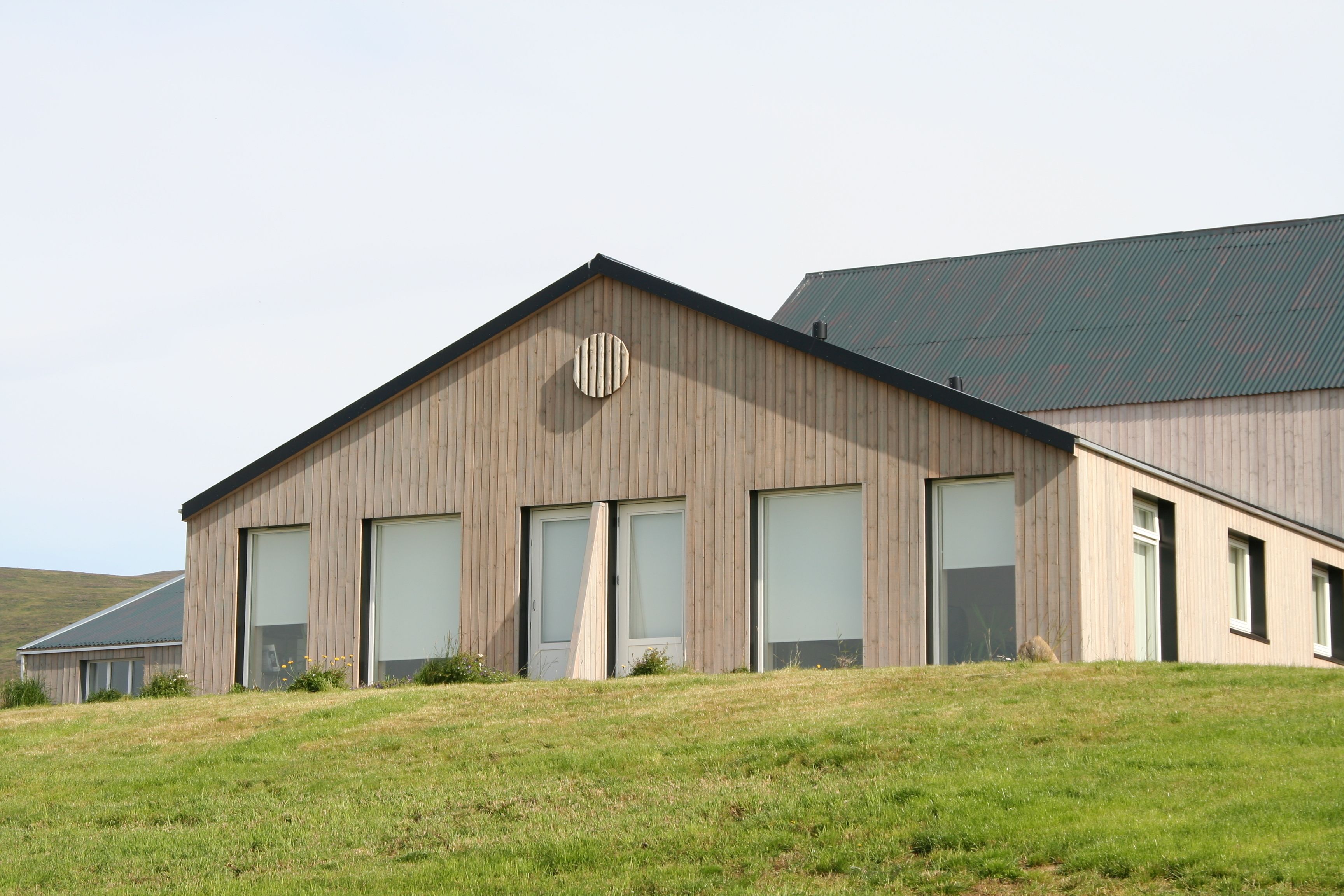 Un bâtiment moderne doté d’un toit en pente, de grandes fenêtres et d’un logo circulaire bien visible sur la façade.