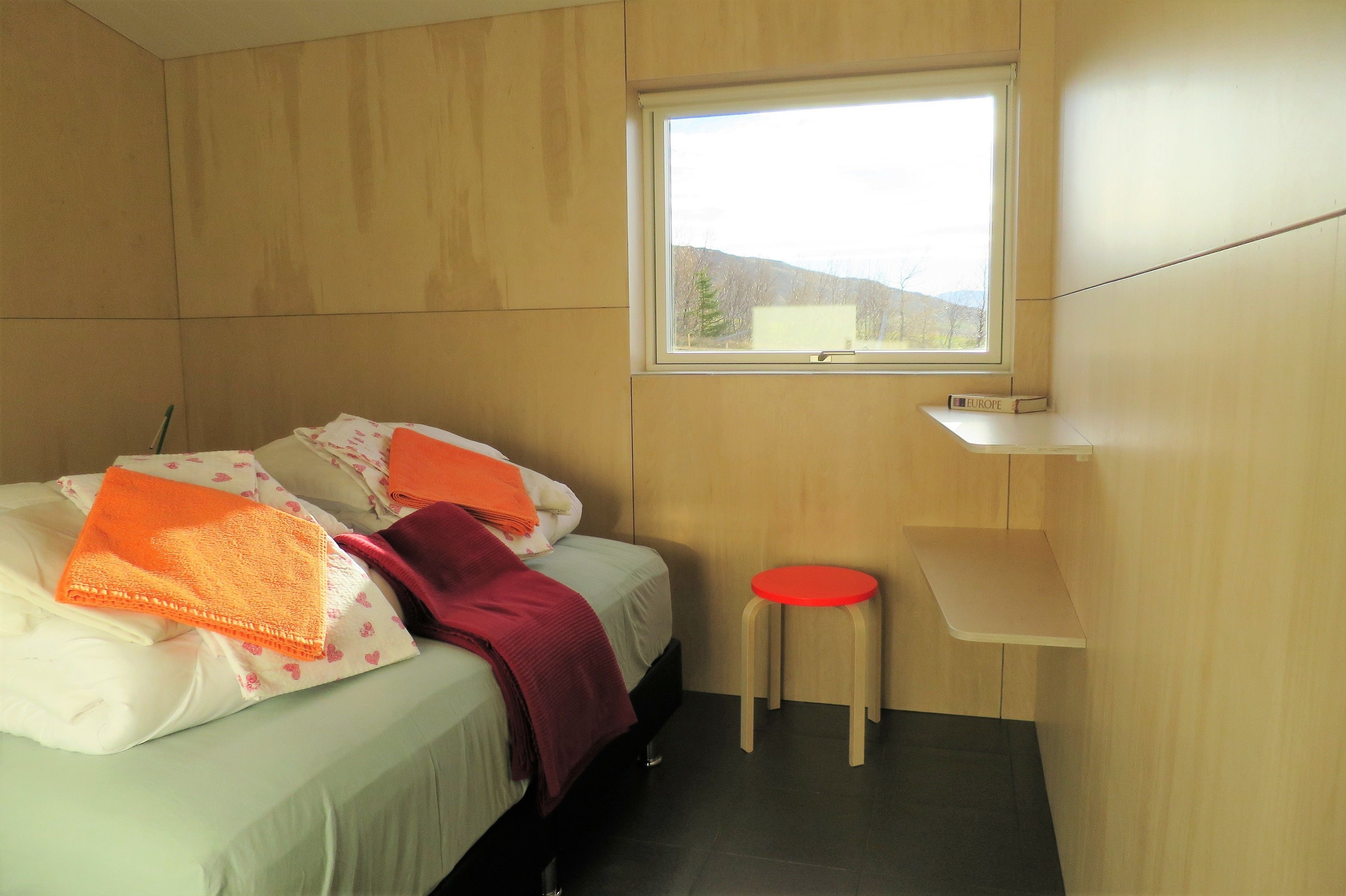 Een kamer met twee bedden, een raam en een klein krukje.