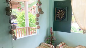 Una habitación acogedora con dos camas individuales, una mesita con mantel morado, un dardo y una ventana con vistas a la vegetación.