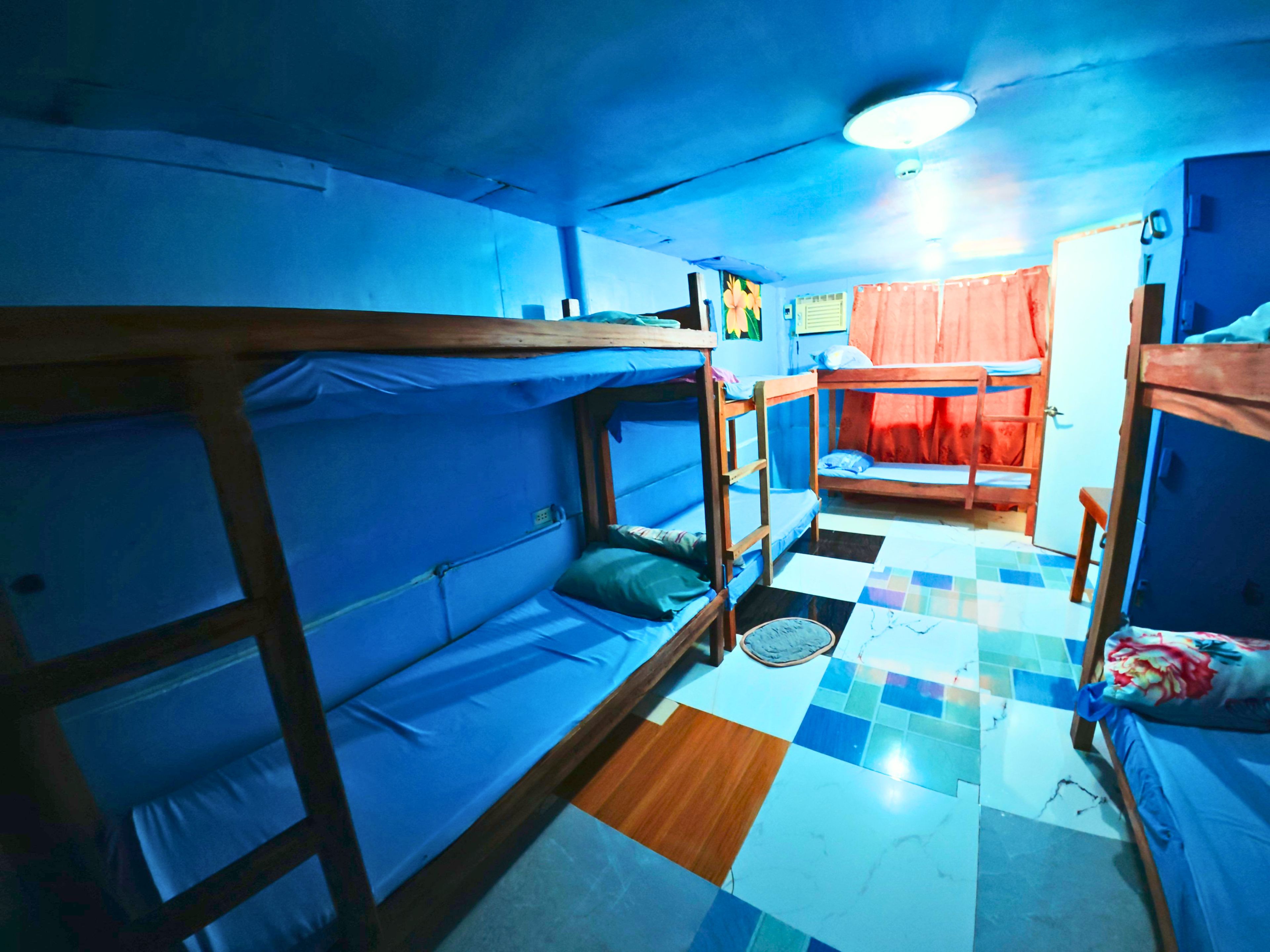 A dormitory room with bunk beds, a tiled floor, and a ceiling fan.
