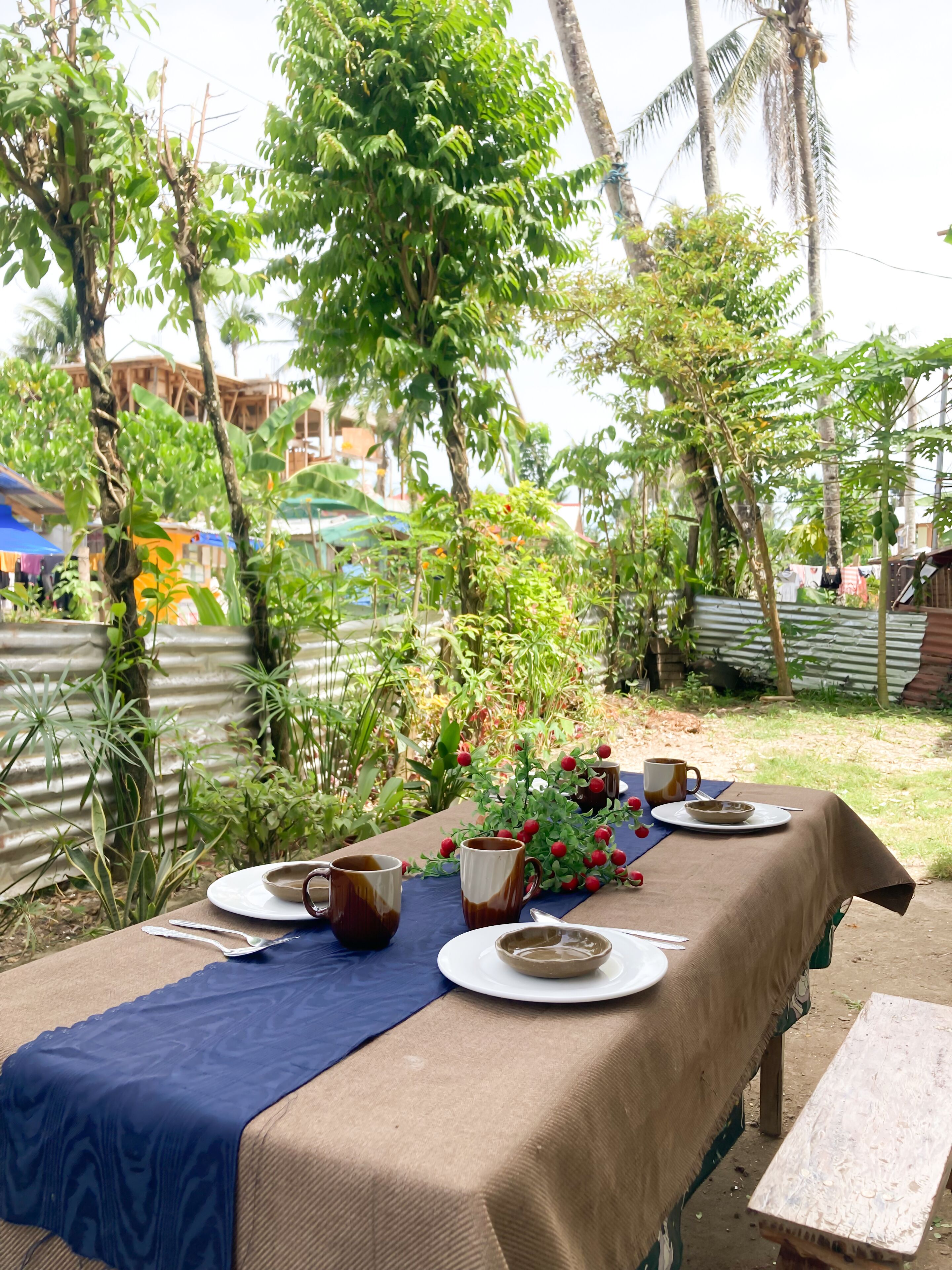 A table set outdoors with a tablecloth, plates, cups, and a bowl.