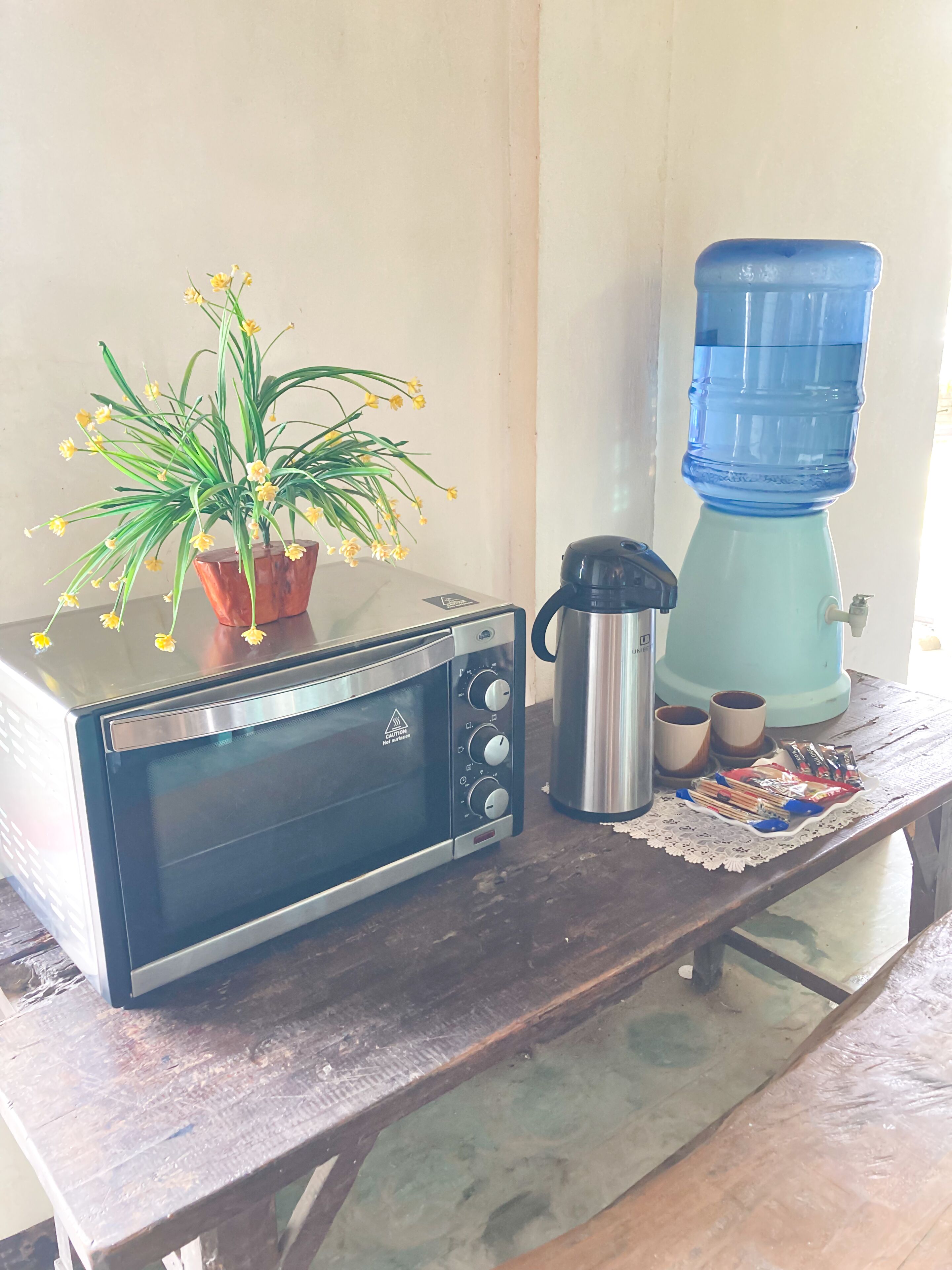 Una cuina amb un taulell, un forn tostatge, un dispensador d'aigua, una cafetera i una petita planta en test.