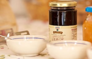 A jar of Ciliegi honey with a spoon and a bowl on a table. - Parco degli Aranci (Cutrofiano)