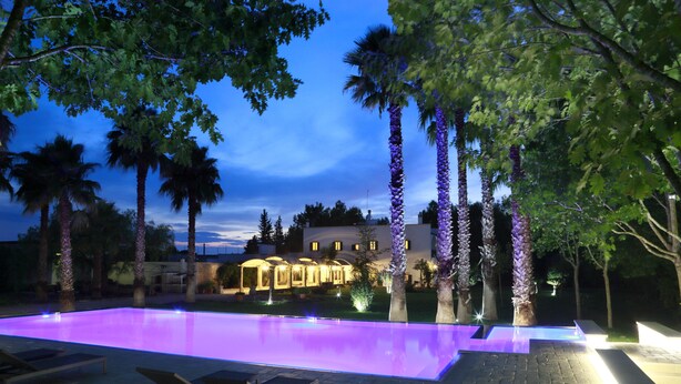 An infinity pool with a purple-lit edge, surrounded by palm trees and lounge chairs. - Parco degli Aranci (Cutrofiano)