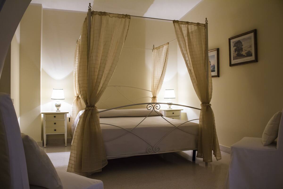 A bedroom with a four-poster bed, two bedside tables, and a nightstand.