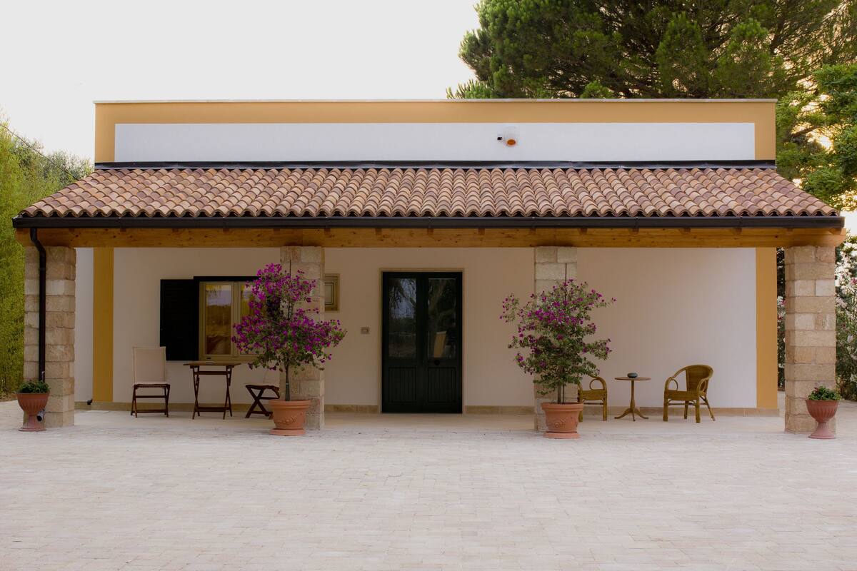 A building with a tiled roof, a black door, and a small patio area with chairs and potted plants.