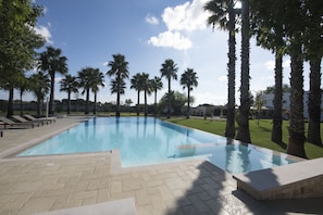 A swimming pool surrounded by palm trees and a grassy area. - Parco degli Aranci (Cutrofiano)